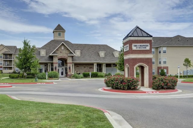 Exterior view of a multifamily community entrance with a brick sign and landscaped roundabout.