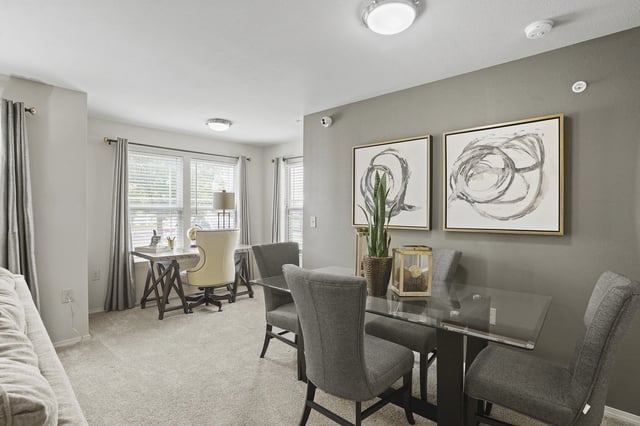 Dining area with a glass-top table and chairs, next to a home office setup with a desk and chair.