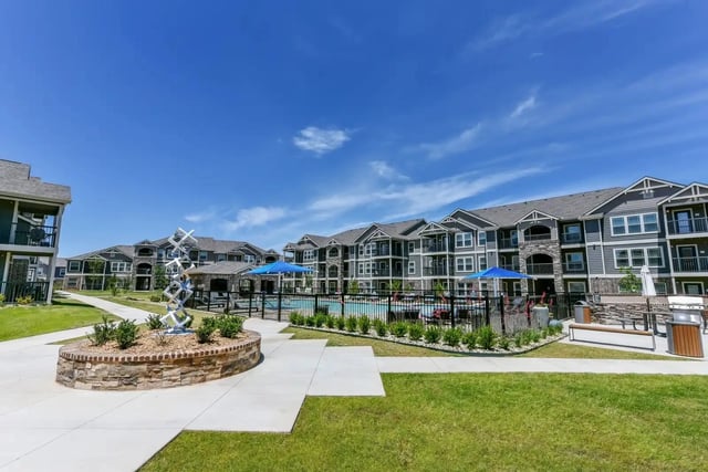 Exterior view of a modern apartment community with a central pool and green courtyard.
