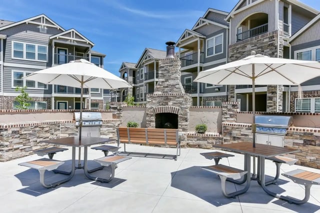 Outdoor community courtyard with a stone fireplace, grills, benches, and umbrellas.