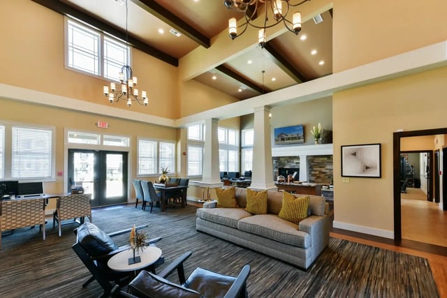 Interior of a modern apartment community lounge with seating, a fireplace, and high ceilings.
