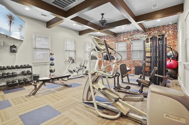 Interior of a residential gym with treadmills, weights, and a brick accent wall.