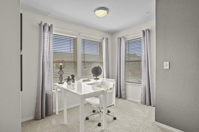 Bright apartment office with a white desk, chair, and three windows with blinds.