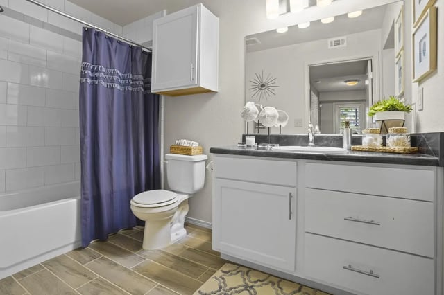 Bathroom in a modern apartment: white vanity with gray countertop, toilet, and a purple shower curtain.