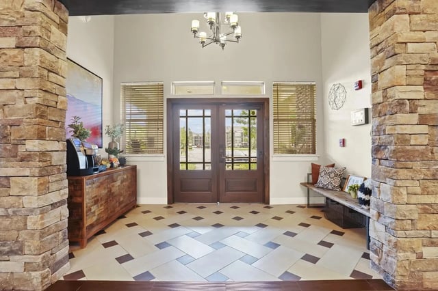 Lobby area with double wooden doors, stone columns, and a patterned tile floor.