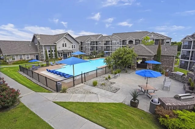 Outdoor pool area at an apartment community with blue umbrellas and lounge chairs.