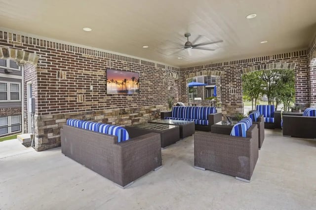 Outdoor covered community lounge with wicker seating and a wall-mounted TV.