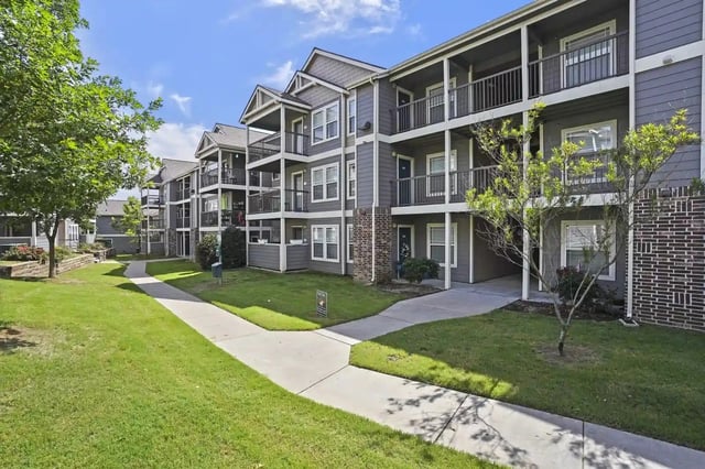 Exterior view of a multi-unit apartment building with balconies and manicured lawn.