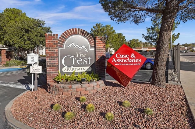 Exterior sign for The Crest Apartments with a red Case & Associates sign, landscaped with rocks.