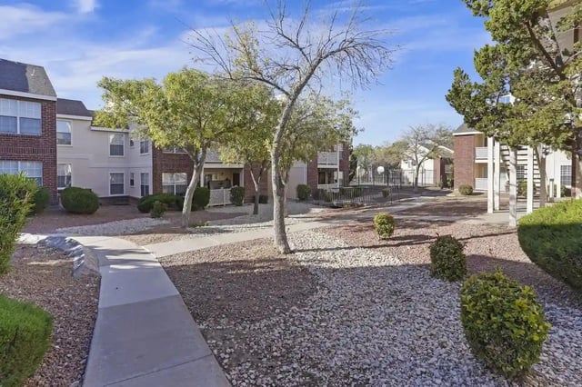 Exterior view of a multi-building apartment community with walkways, trees, and desert landscaping.