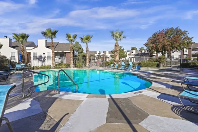 Outdoor apartment community pool with blue lounge chairs and palm trees.
