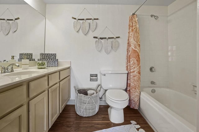 Bathroom with long beige vanity, toilet, and bathtub with orange-pattern curtain.