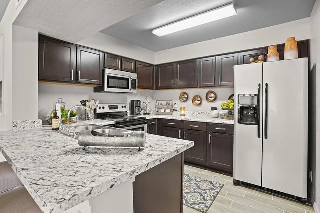 Modern kitchen with dark wood cabinets, granite countertops, stainless steel appliances, and a large refrigerator.