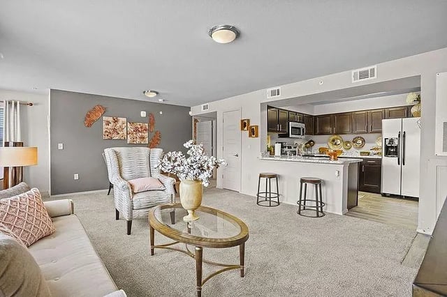 Living room and kitchen area with white sofa, armchair, coffee table, and bar stools.