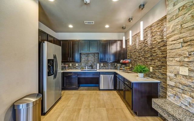 Modern apartment kitchen with dark cabinets, stainless steel appliances, and stone accent wall.