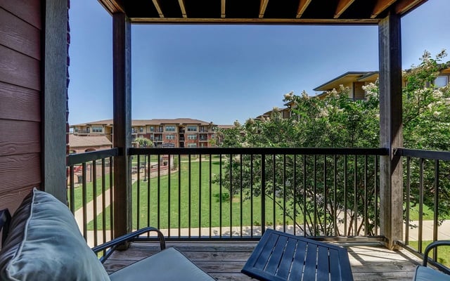Balcony with seating overlooks a lush courtyard and surrounding apartment buildings.