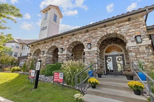 Exterior view of a stone-clad apartment entrance with arches and landscaping.