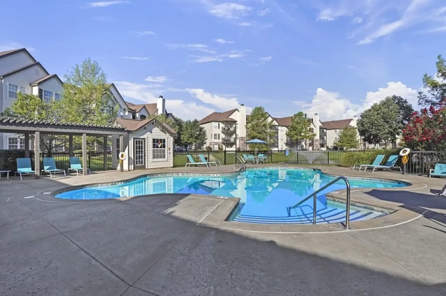 Outdoor apartment community pool with lounge chairs and a small pool house.