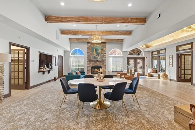 Spacious community lounge with round table, chairs, stone fireplace, and arched windows.