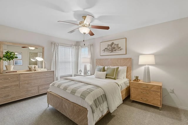 King-size bed with green and white bedding in a bright bedroom with a dresser and a ceiling fan.