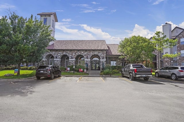 Exterior view of a stone-clad apartment building with arched entrances and a parking lot.