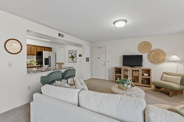 Living room with a white sectional sofa, a TV on a stand, and a kitchen area with bar stools.