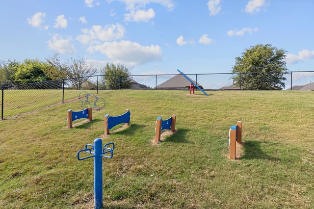Dog park with agility equipment and a seesaw under a blue sky with clouds.