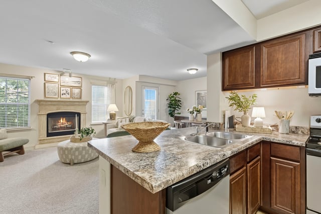 View of a kitchen island with a sink and dishwasher, overlooking a living area with a fireplace and seating.