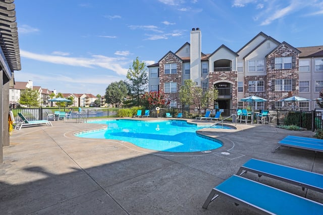 Resort-style swimming pool with lounge chairs and umbrellas at an apartment complex.