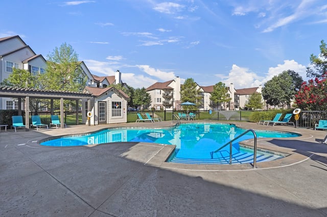 Outdoor swimming pool with lounge chairs and tables at a multifamily property.