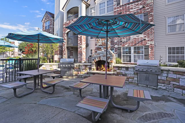 Outdoor grilling and fireplace area with picnic tables and umbrellas.