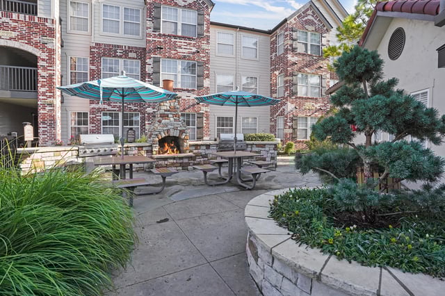 Outdoor patio area with a stone fireplace, grill, and seating under umbrellas.