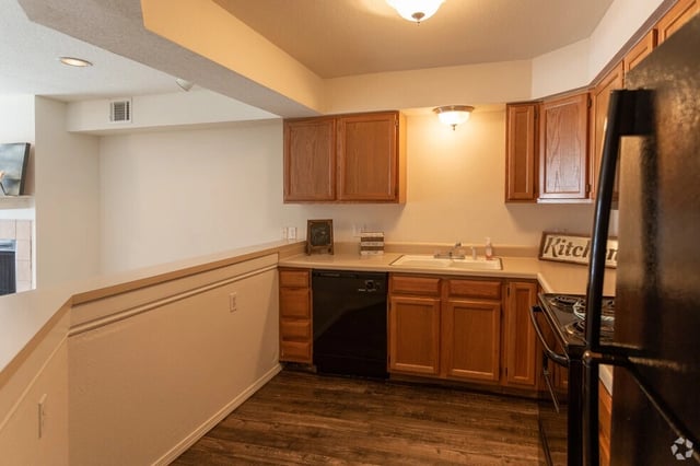 Kitchen with wooden cabinets, black dishwasher, sink, and stove.