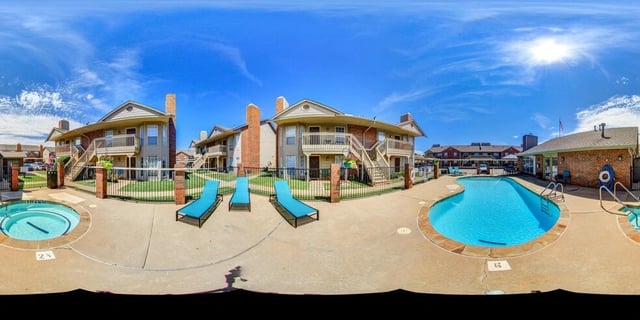 Resort-style pool and spa area with lounge chairs and apartment buildings in the background.