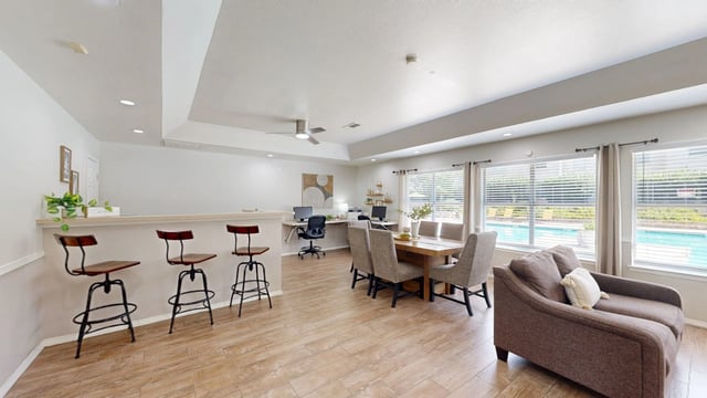 Spacious apartment living area with a dining table, desk area, and bar seating with a view of the pool.