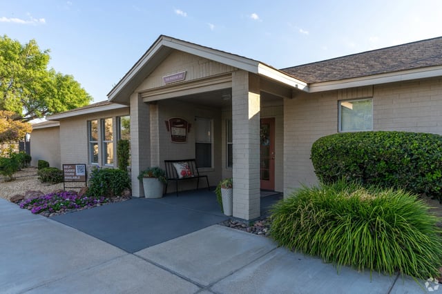 Exterior of a multifamily property with a covered entrance, bench, and landscaping.