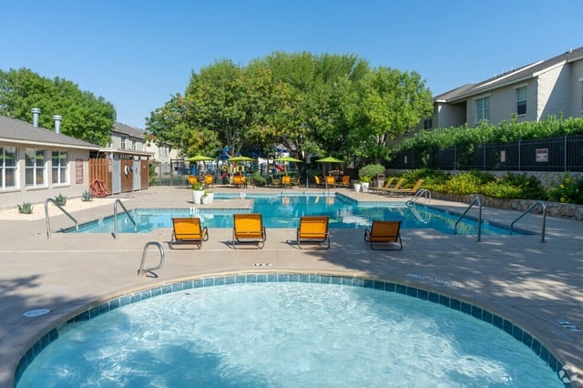 Outdoor swimming pool with lounge chairs and umbrellas, adjacent to a playground area.