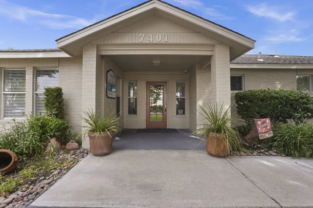 Building entrance with address 7401, porch with potted plants and landscaping.