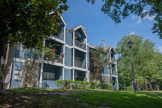 Blue multi-story apartment building exterior with balconies and surrounding trees.