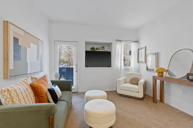 Bright living room in a modern apartment with a green sofa, white chair, TV, and sheer-curtains window.
