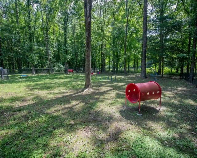 Outdoor playground in a wooded area with a red tunnel play structure and trees.