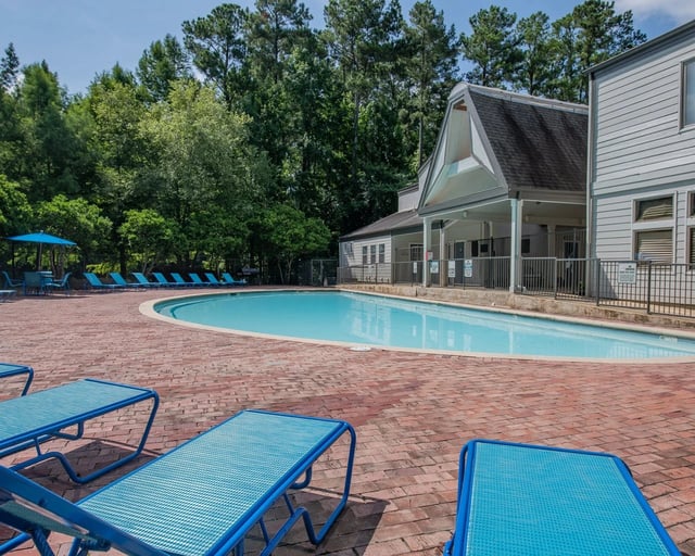 Outdoor community pool with blue lounge chairs on a brick deck beside a building.