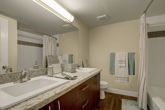 Bathroom with double vanity, granite countertops, and striped shower curtain.