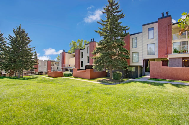 Exterior view of apartment buildings with manicured lawns and trees.