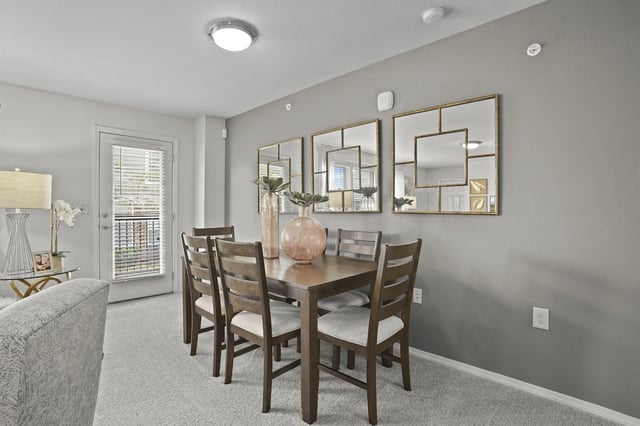Dining room with a wooden table and four chairs, decorative mirrors on the wall, and a door leading to a balcony.