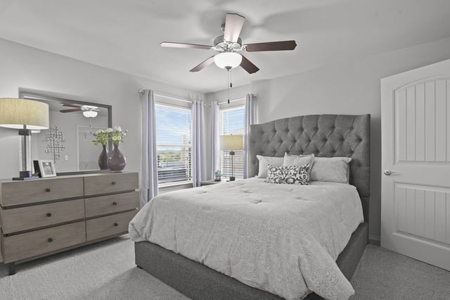 A bedroom with a large bed, a dresser, and a ceiling fan.