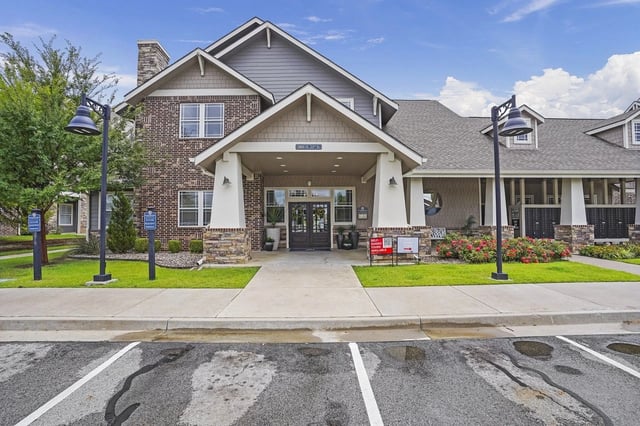 Exterior view of a modern apartment community entrance with brick façade, columns, and landscaping.