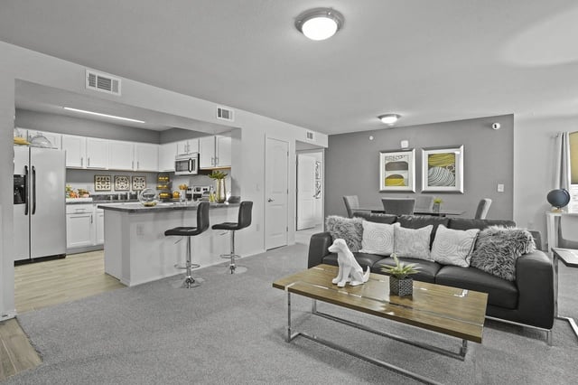 Open-concept living room and kitchen with an island, white cabinets, and a gray sofa.
