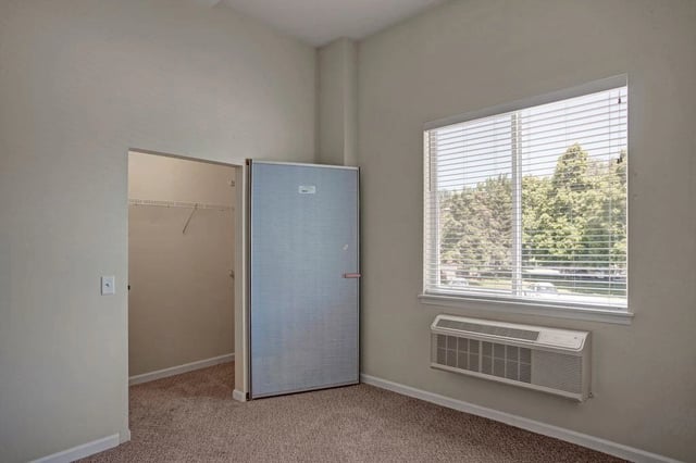 Interior view of a closet and a room with a window and air conditioning unit.