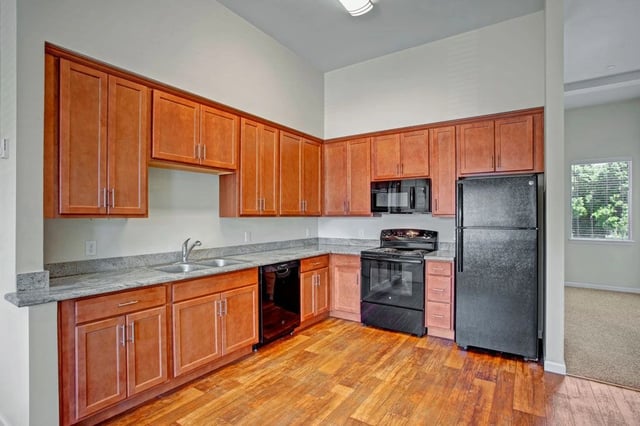 Kitchen with wood cabinets, granite countertops, black appliances, and hardwood floors.